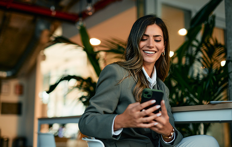 A young woman is sitting in a café, browsing the career services website on her mobile phone.