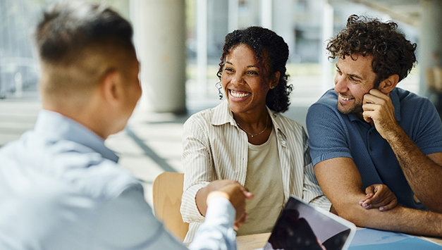 Three people are conversing. A woman shakes a man's hand.