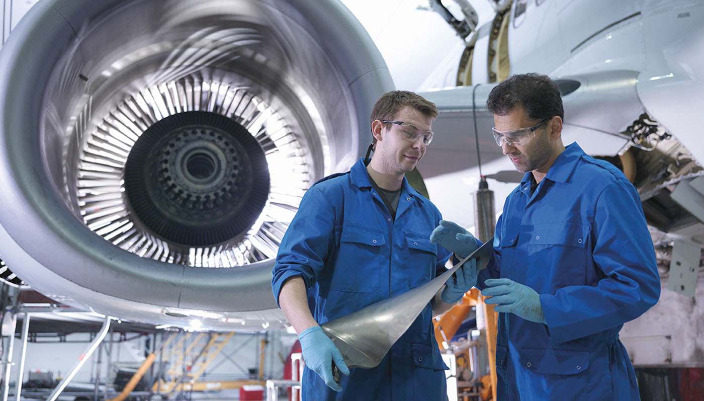 Mechanics stand in an airplane hangar and discuss